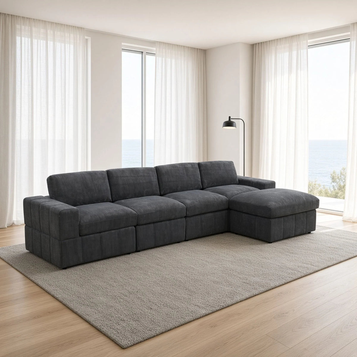 Angled view of a dark gray modular sofa with an ottoman chaise beside tall windows
