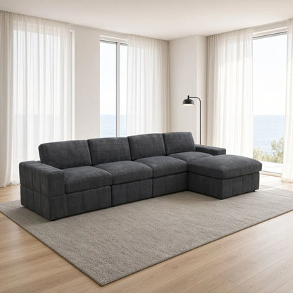 Angled view of a dark gray modular sofa with an ottoman chaise beside tall windows
